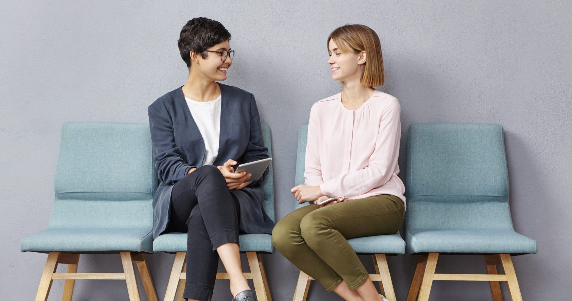Lively conversation in queue. Two unemployed attractive young women in strict clothing talking to each other at HR department and discussing their resumes while waiting their turn for job interview